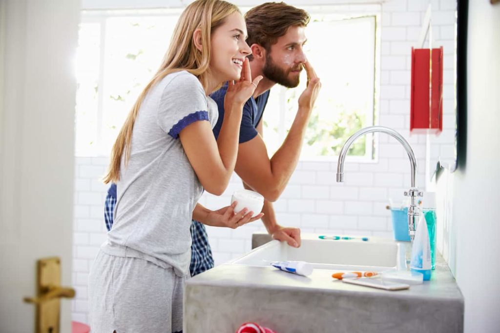 woman and man in front of mirror performing daily skincare routine